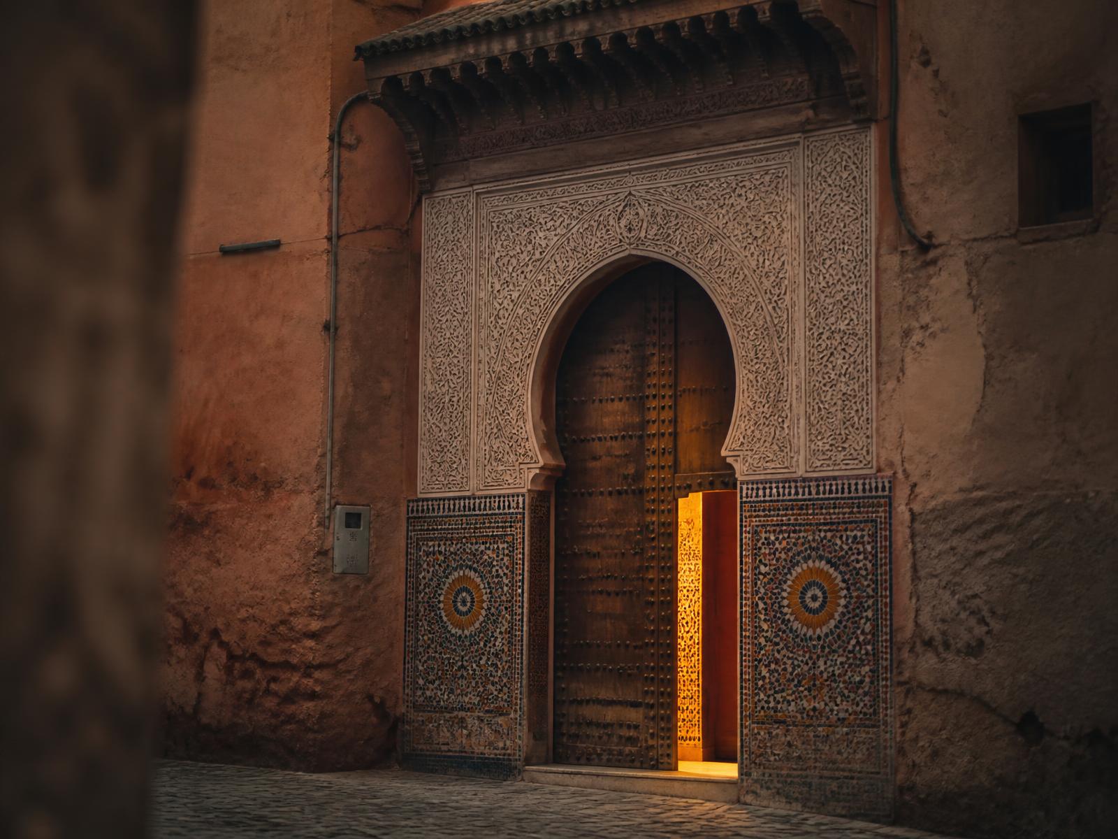 An ornate Moroccan door standing slightly ajar, warm light spilling out